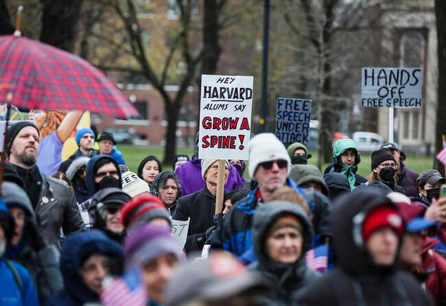 Protesters hold signs imploring Harvard University to resist the demands of President Trump's administration.